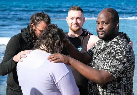 Believers laying hands on one another in prayer beside the sea